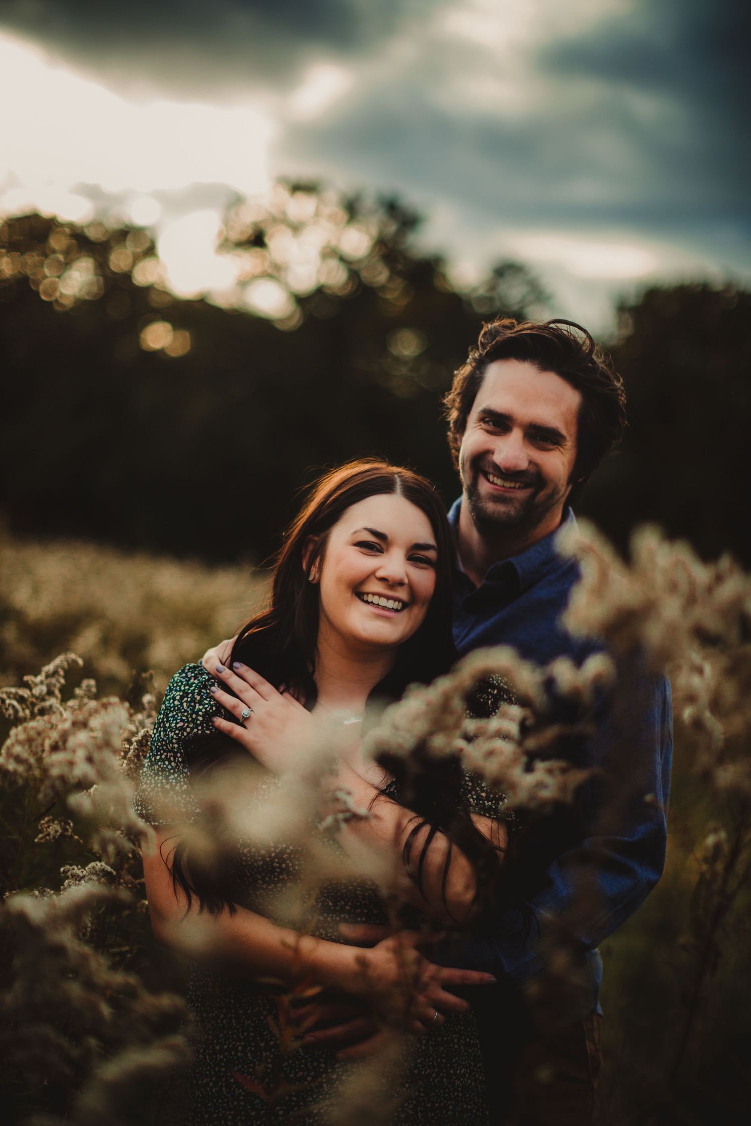 Joyful couple holding chihuahua dog during outdoor sunset photo session.