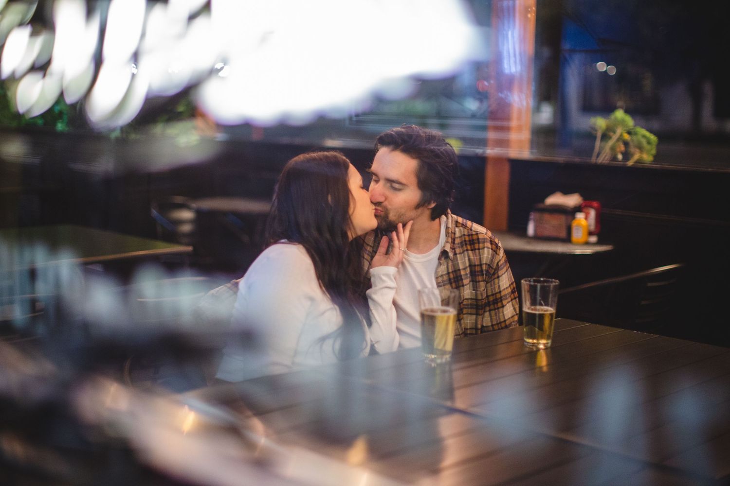 Intimate couple sharing a romantic kiss at a dimly lit restaurant table.