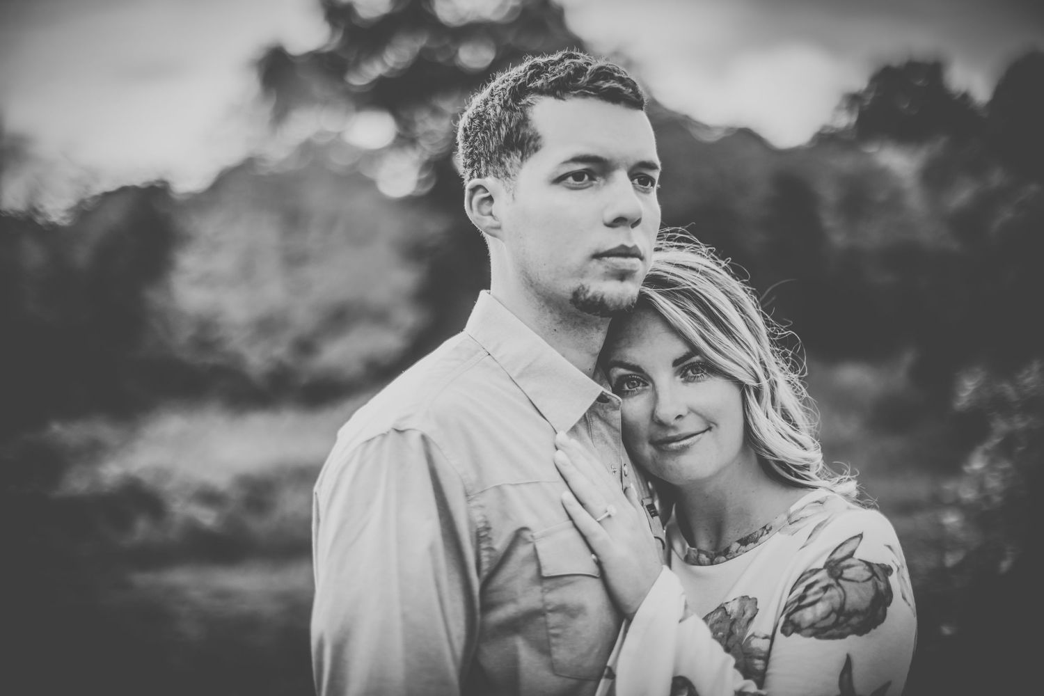 Black and white portrait of a couple embracing against a moody sky.