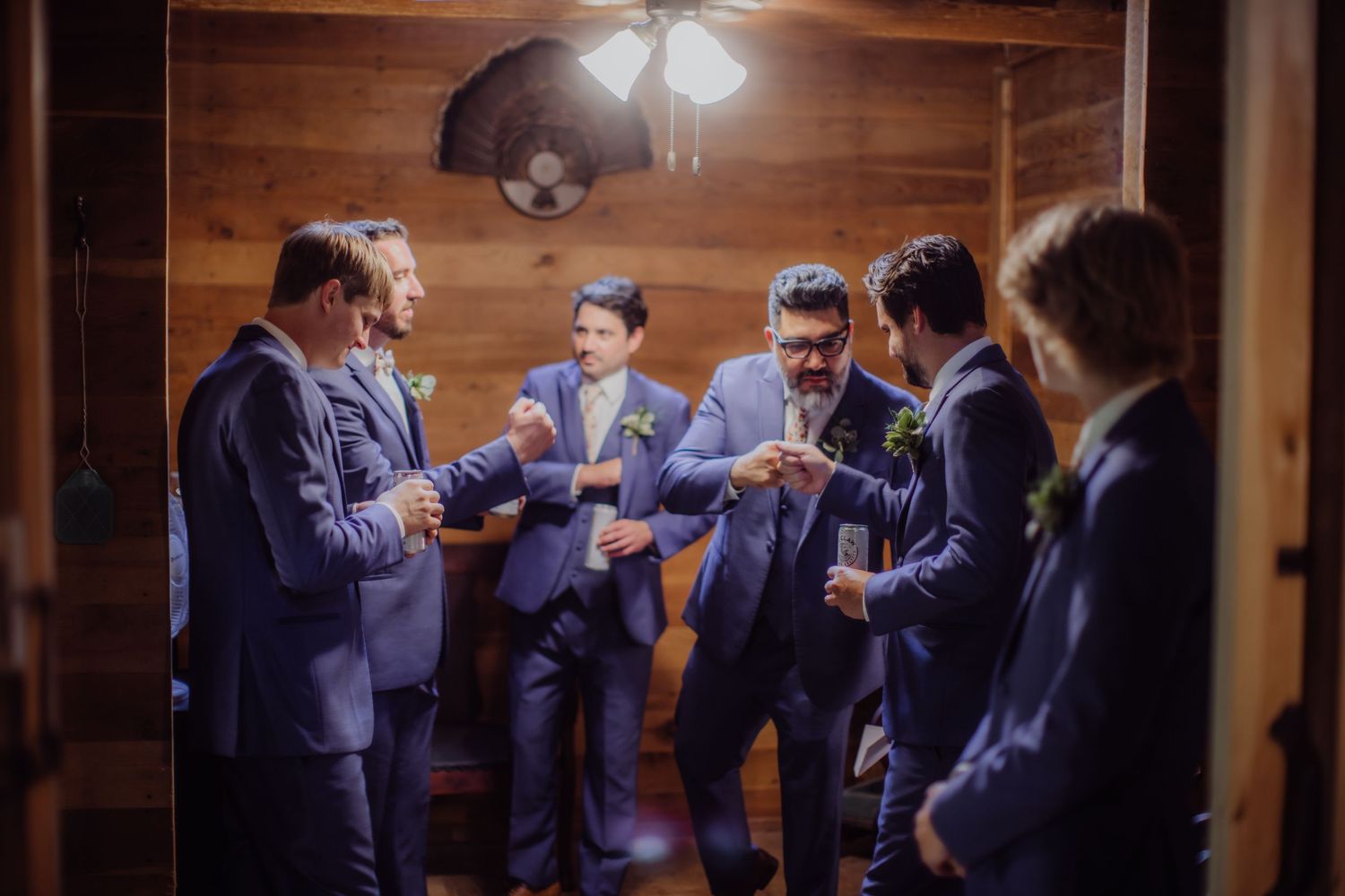 Group of groomsmen in navy suits gather in rustic wooden room.