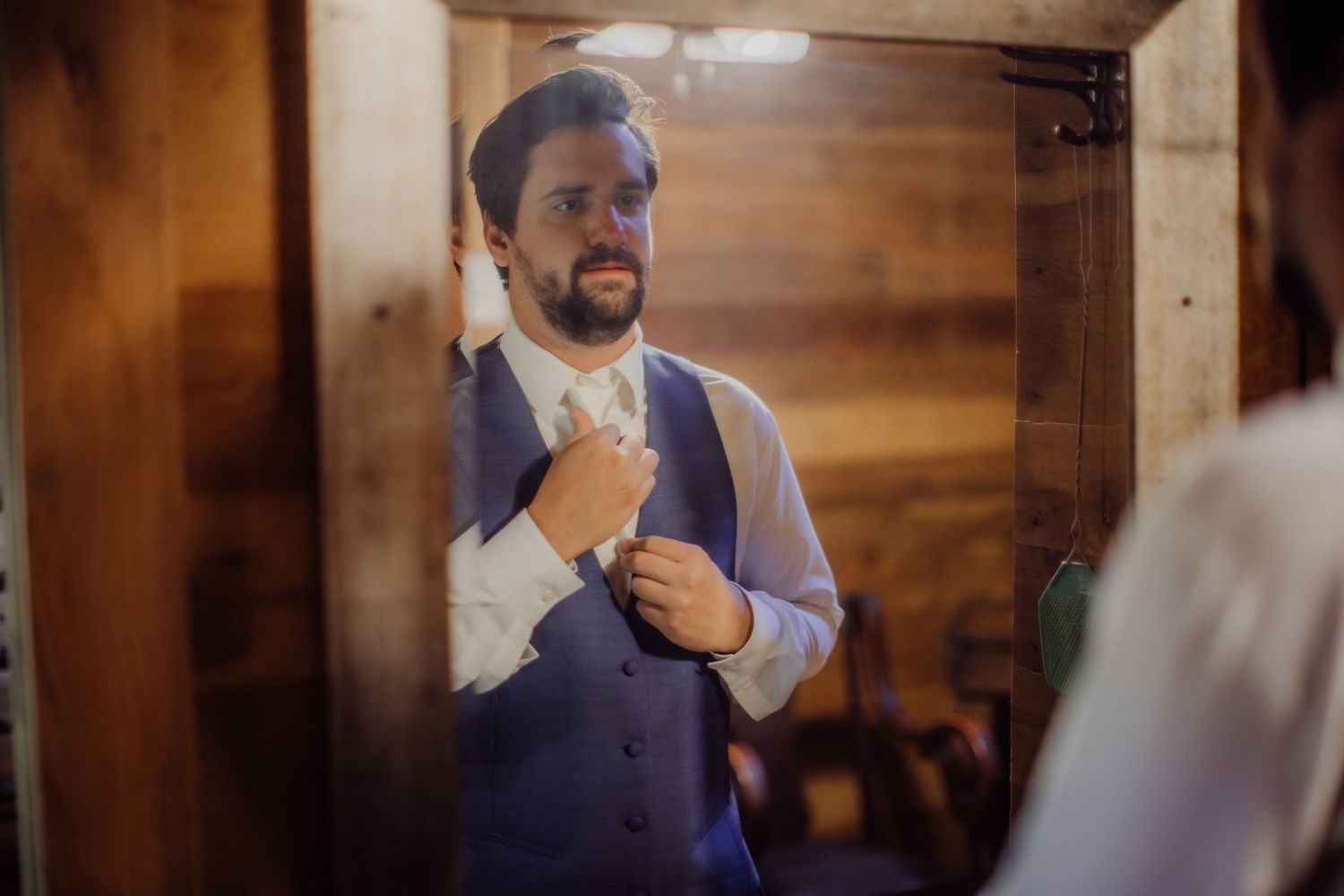 Person in purple vest and white shirt adjusting tie while looking in mirror.