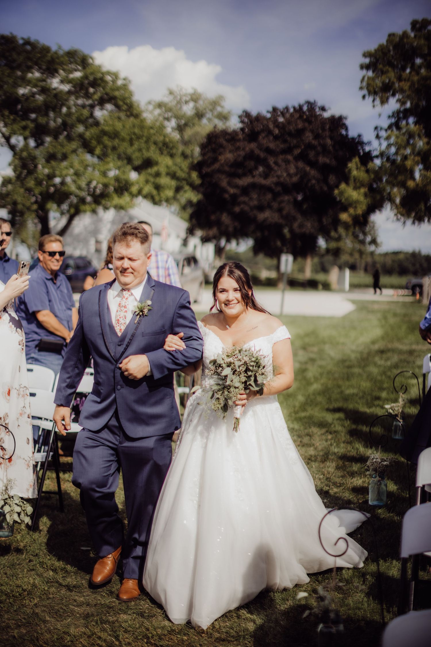 Wedding party walking together during outdoor ceremony with trees and blue sky.