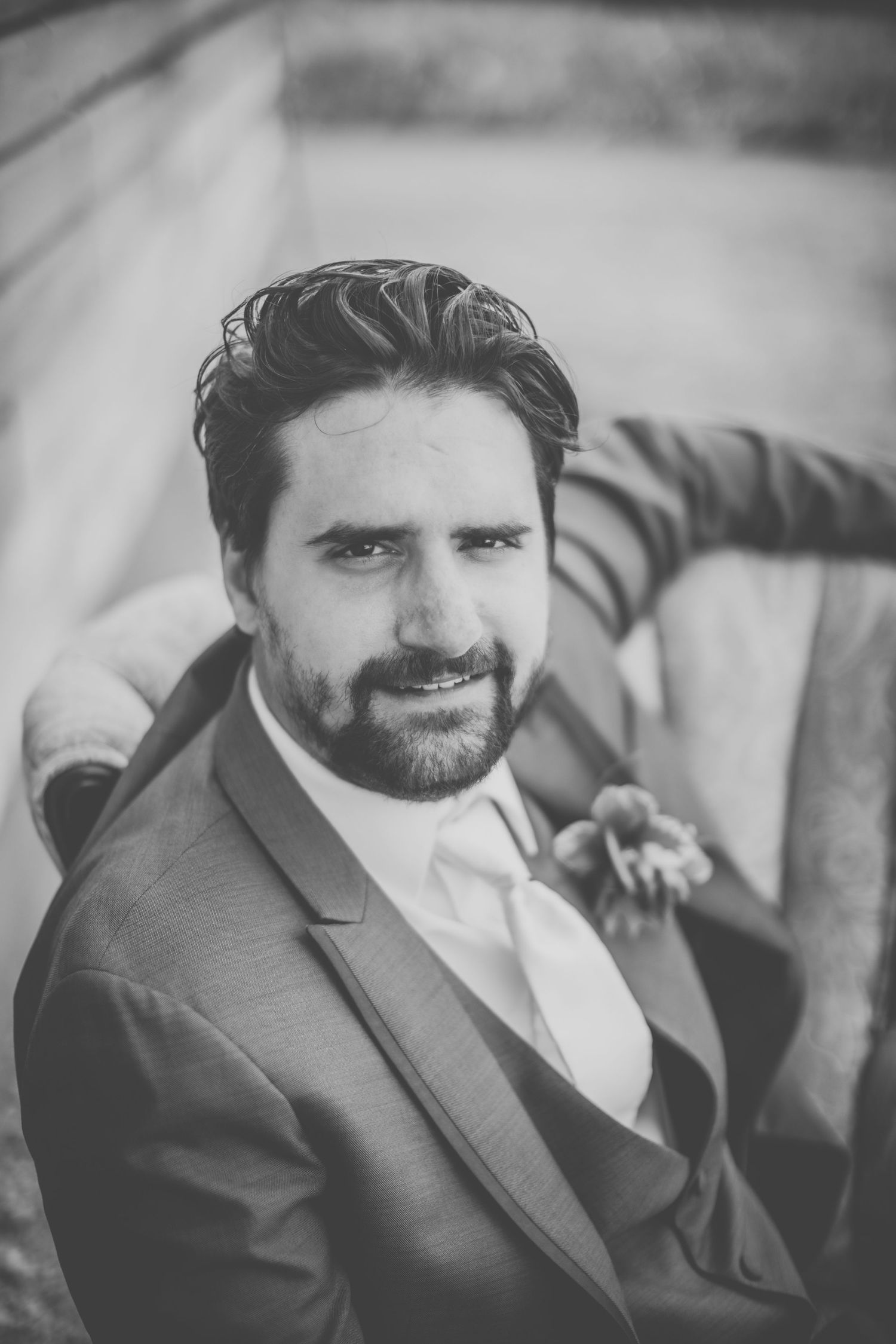 Black and white close-up portrait of a bearded groom in a suit with a boutonniere.