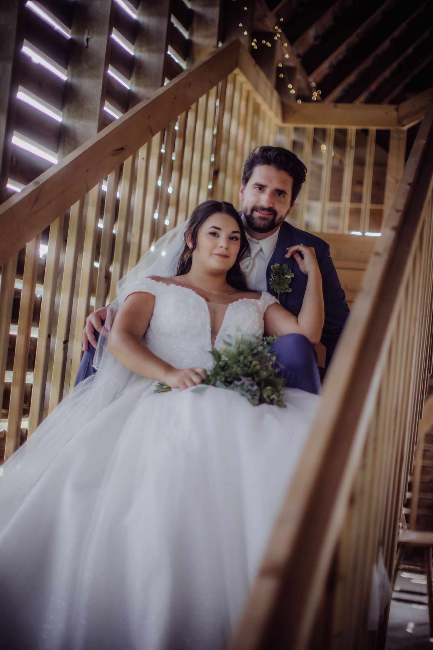 Wedding couple poses on illuminated wooden staircase with string lights in background.