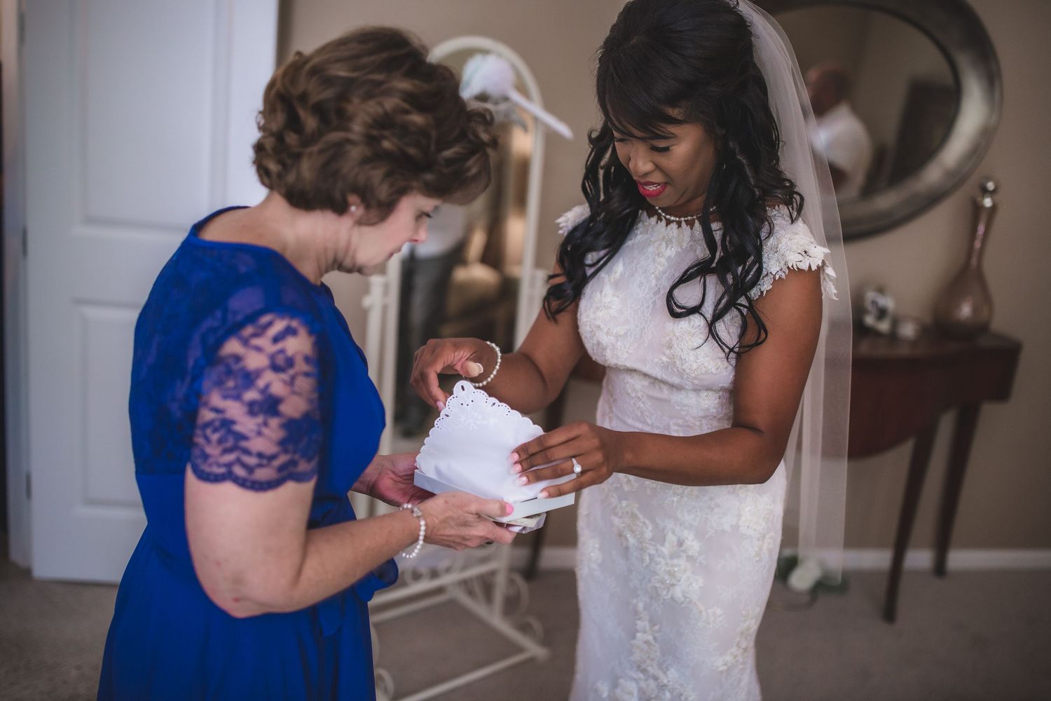 Two women review wedding details while standing in a room with an ornate mirror.