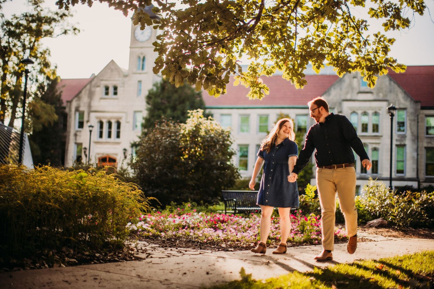 A couple strolls along a campus walkway during autumn with historic architecture behind them.
