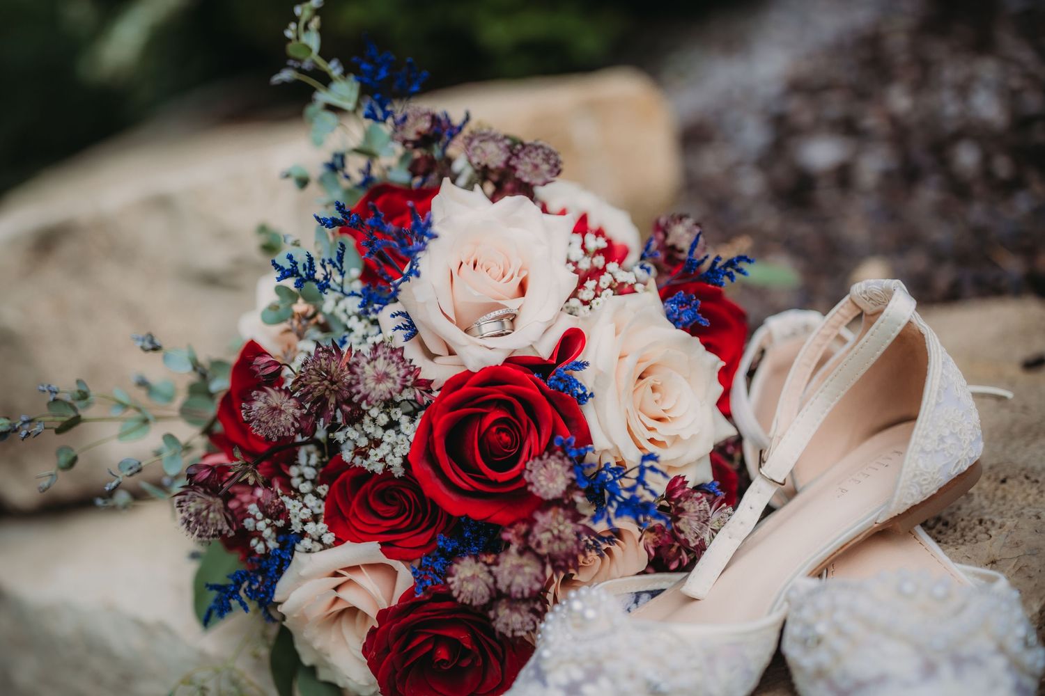 Romantic bridal bouquet featuring red and blush roses with navy accents alongside white shoes.