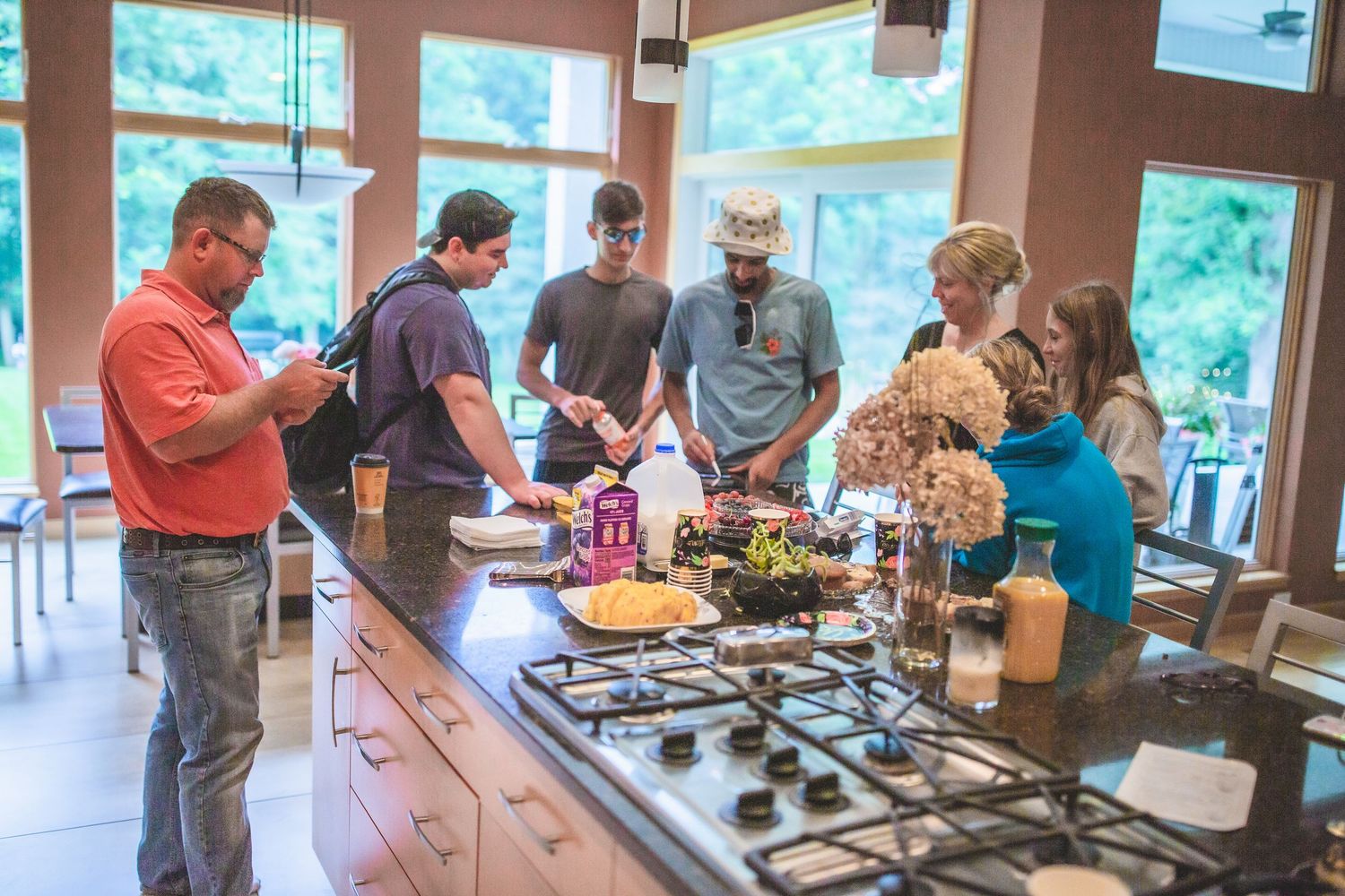 Group of guests socializing around a kitchen island with food and drinks.