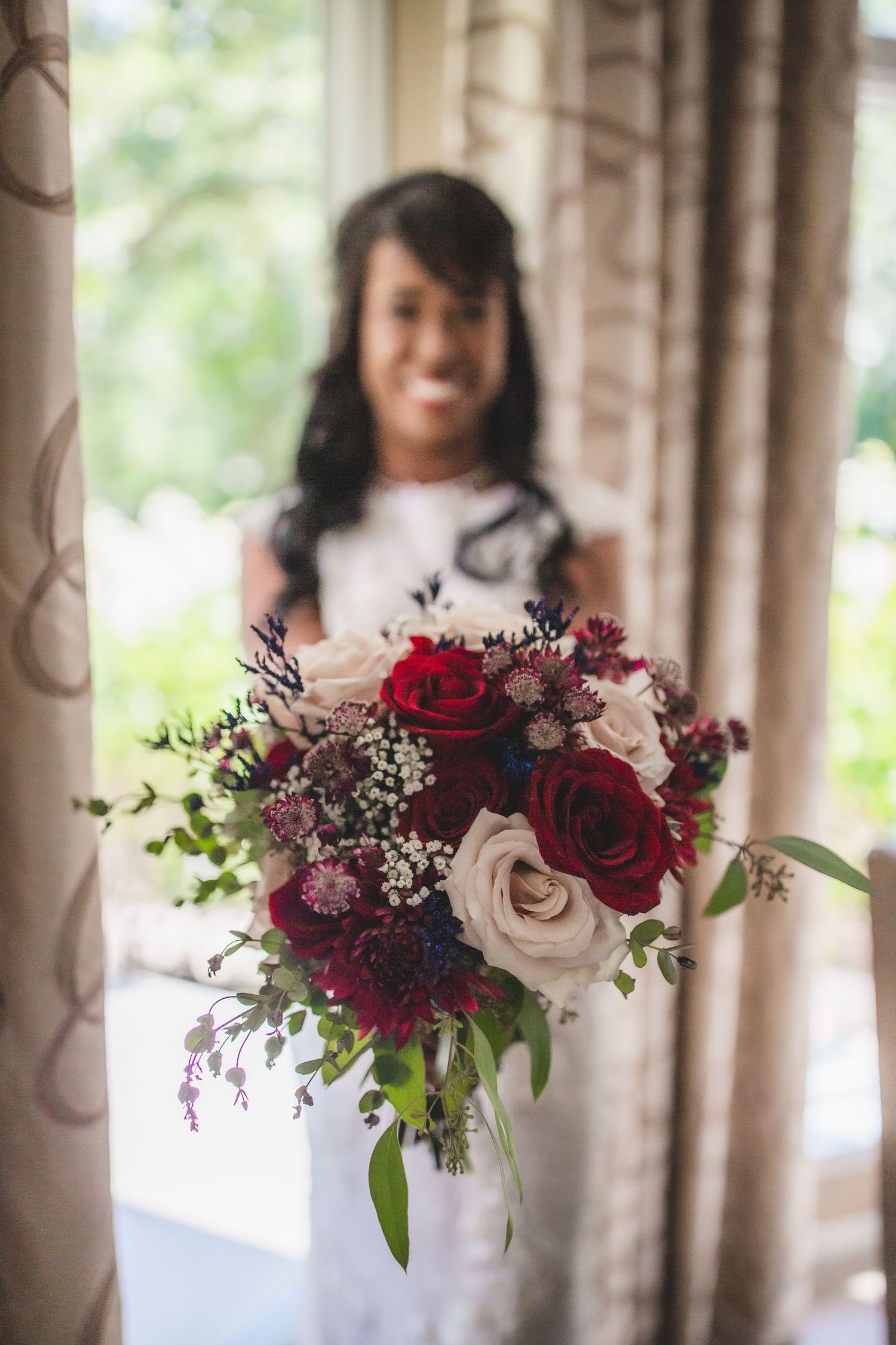 A close-up of a wedding bouquet featuring deep red and blush roses with greenery.