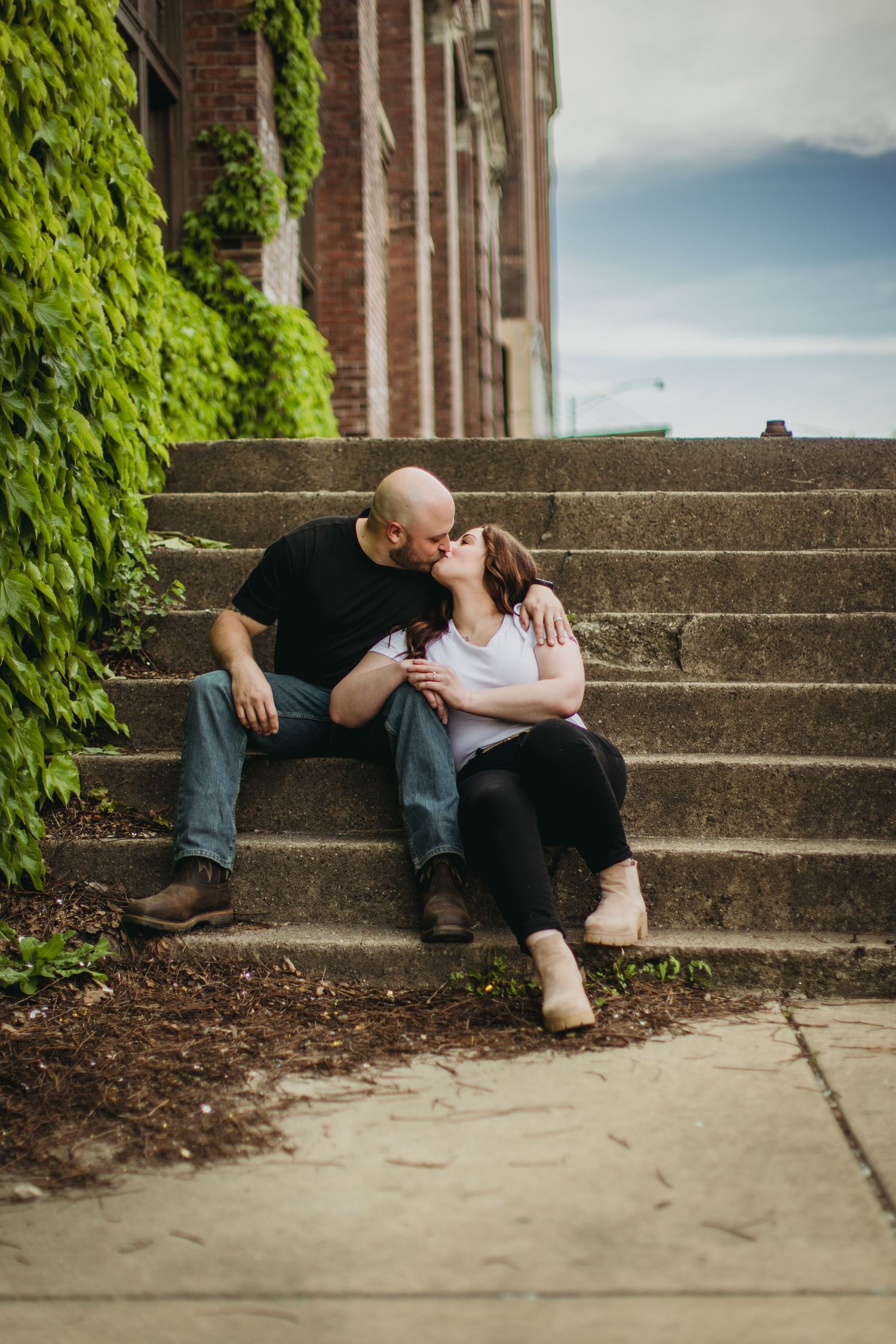 Romantic couple sharing tender moment while sitting on stone steps near ivy-covered wall.