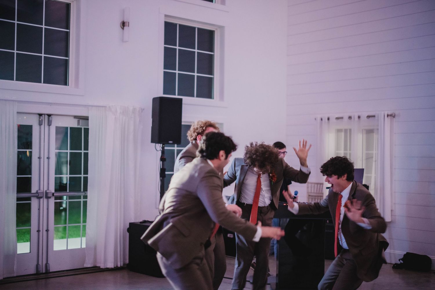 Group of party guests dancing together at an elegant indoor venue with white walls and windows.