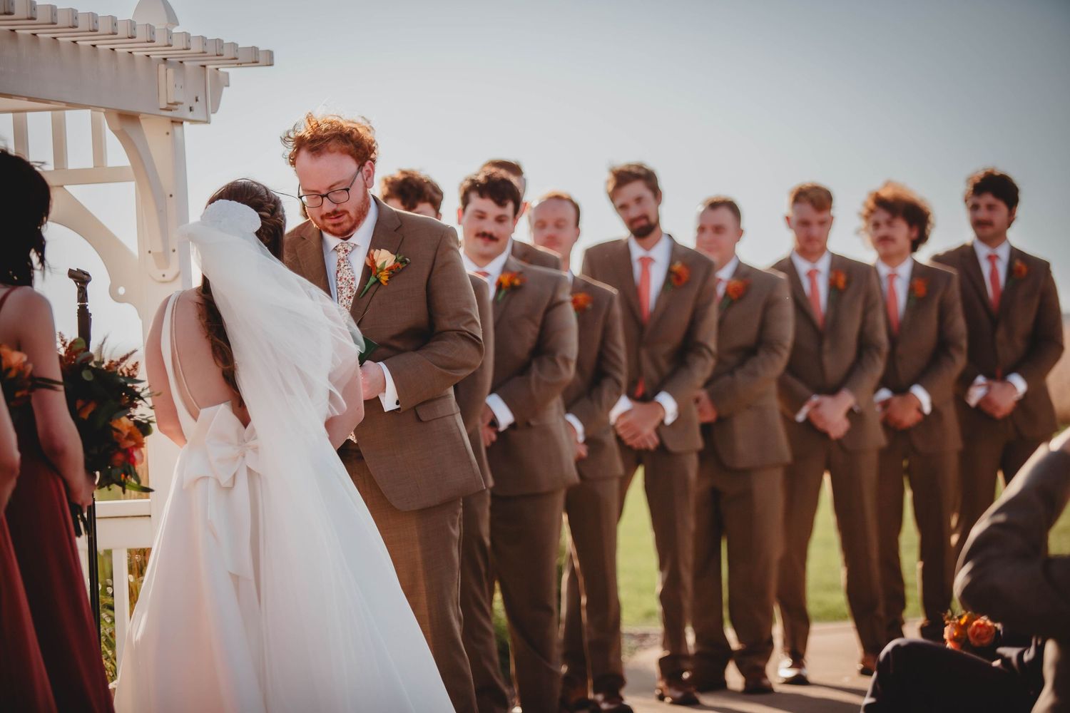 Wedding party lined up under white pergola during outdoor ceremony.