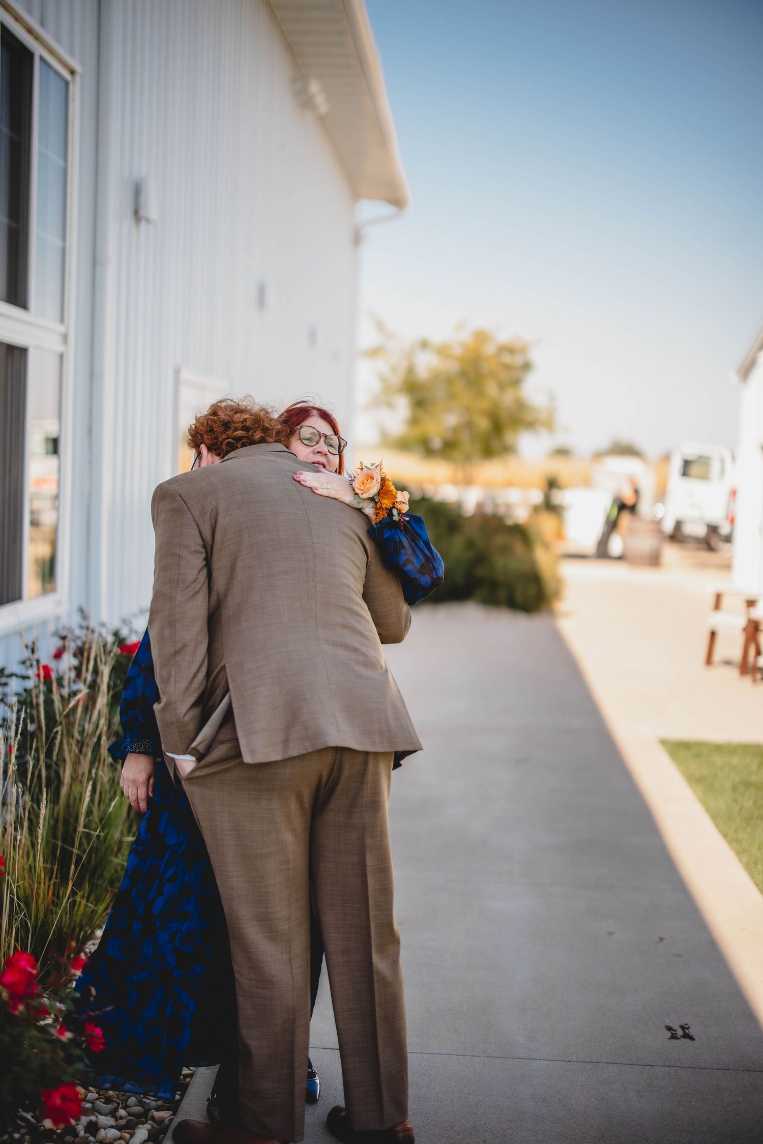 A couple embracing on a sidewalk next to red flowers.