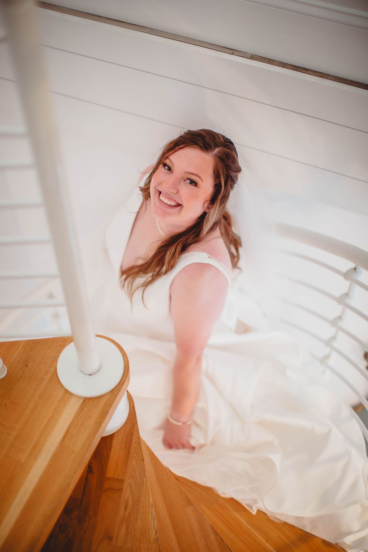 A person in a white wedding dress twirls on wooden stairs.