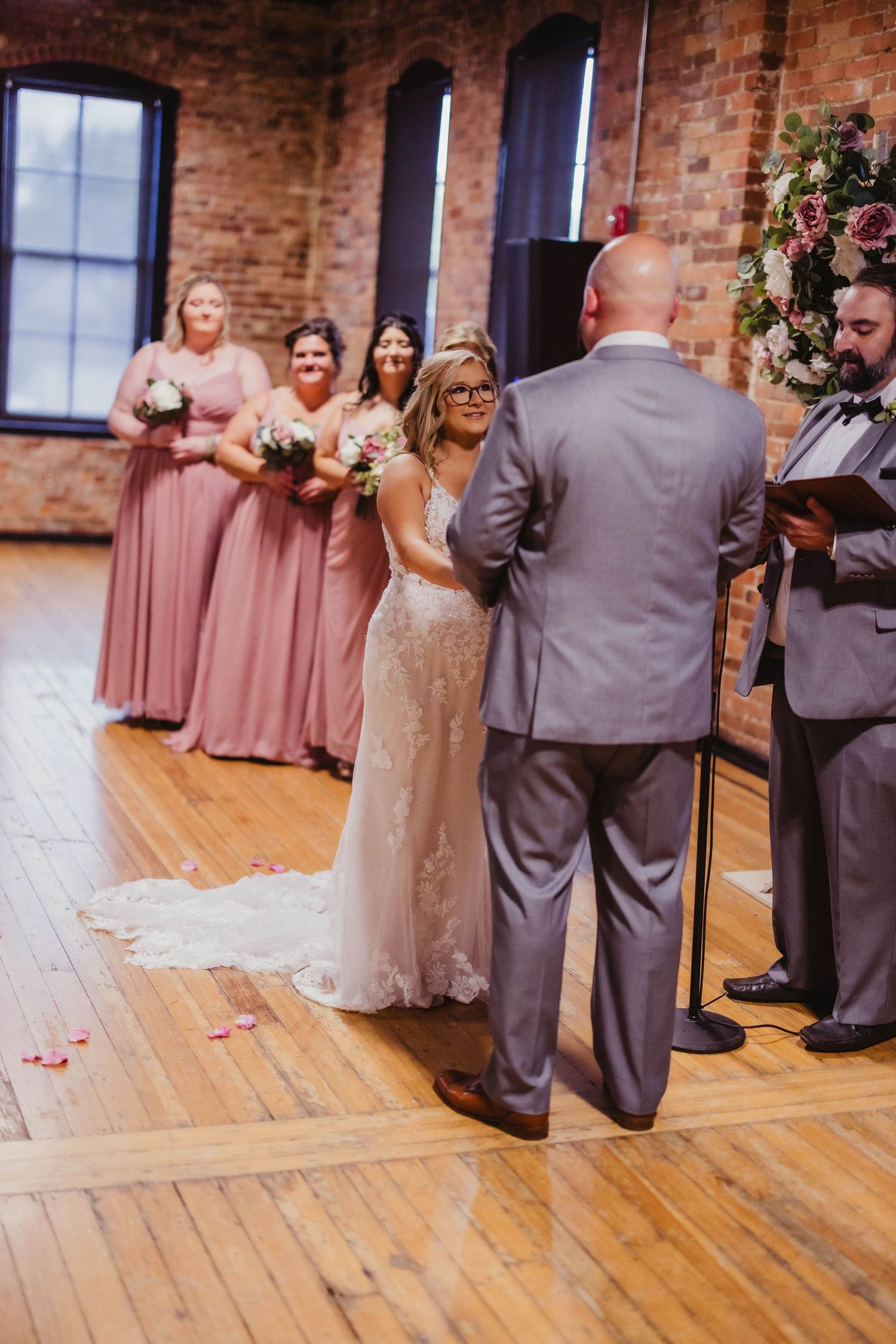 Wedding ceremony with bridesmaids in pink dresses and exposed brick wall backdrop.