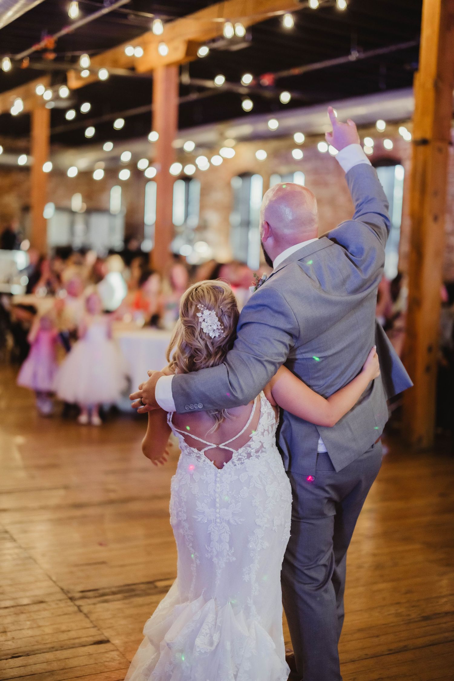 Joyful wedding dance captured under string lights in rustic brick venue.