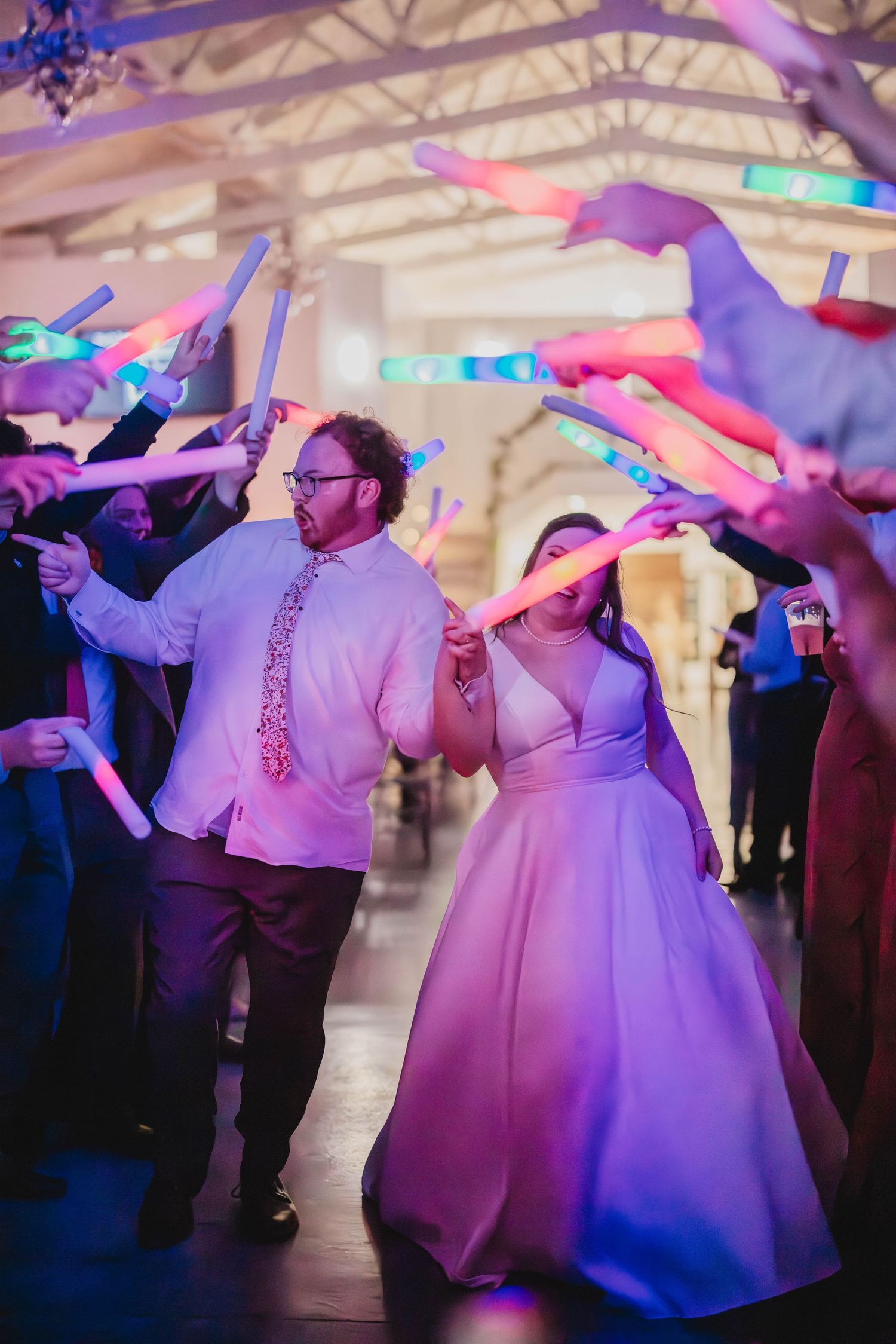 Reception guests create tunnel of colorful light sticks as newlyweds dance beneath.