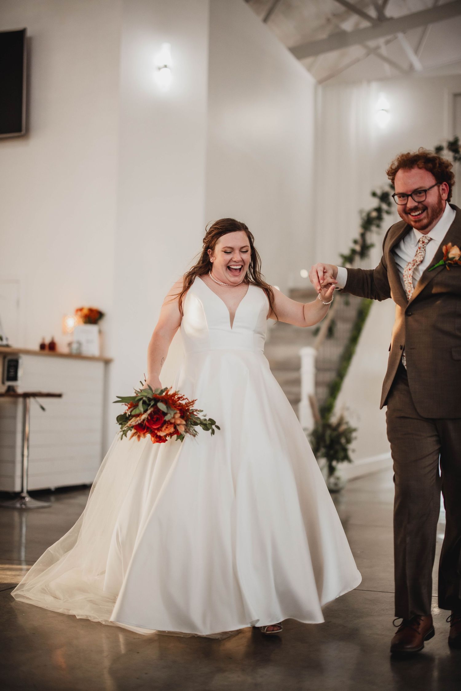 A couple shares a lively dance moment during their wedding celebration in a modern white reception space.