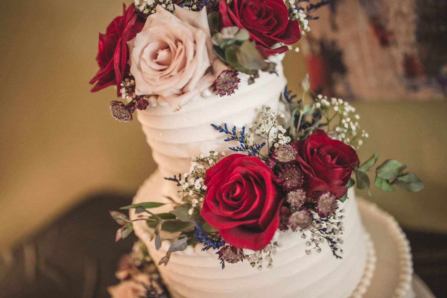 Romantic floral decoration featuring red and pink roses on white wedding cake tiers.