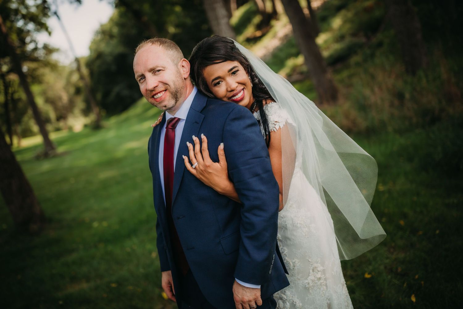 A joyful newlywed couple laughs together during their outdoor wedding photoshoot.
