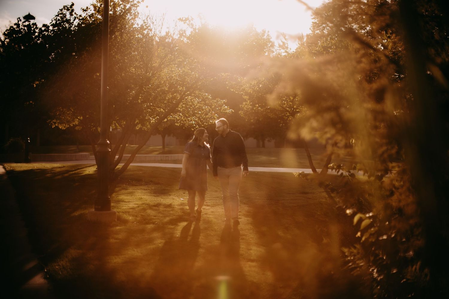Silhouettes of two people walking together at sunset with golden sun flares.