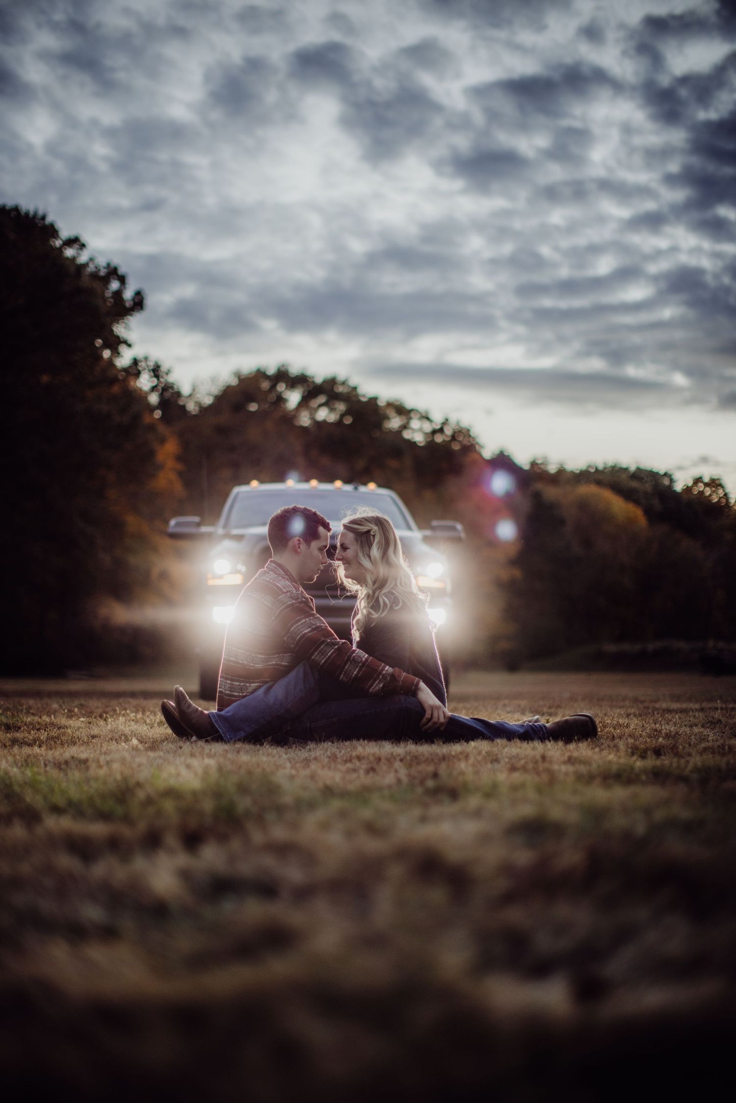 A silhouetted couple shares an intimate moment in front of truck headlights at dusk.