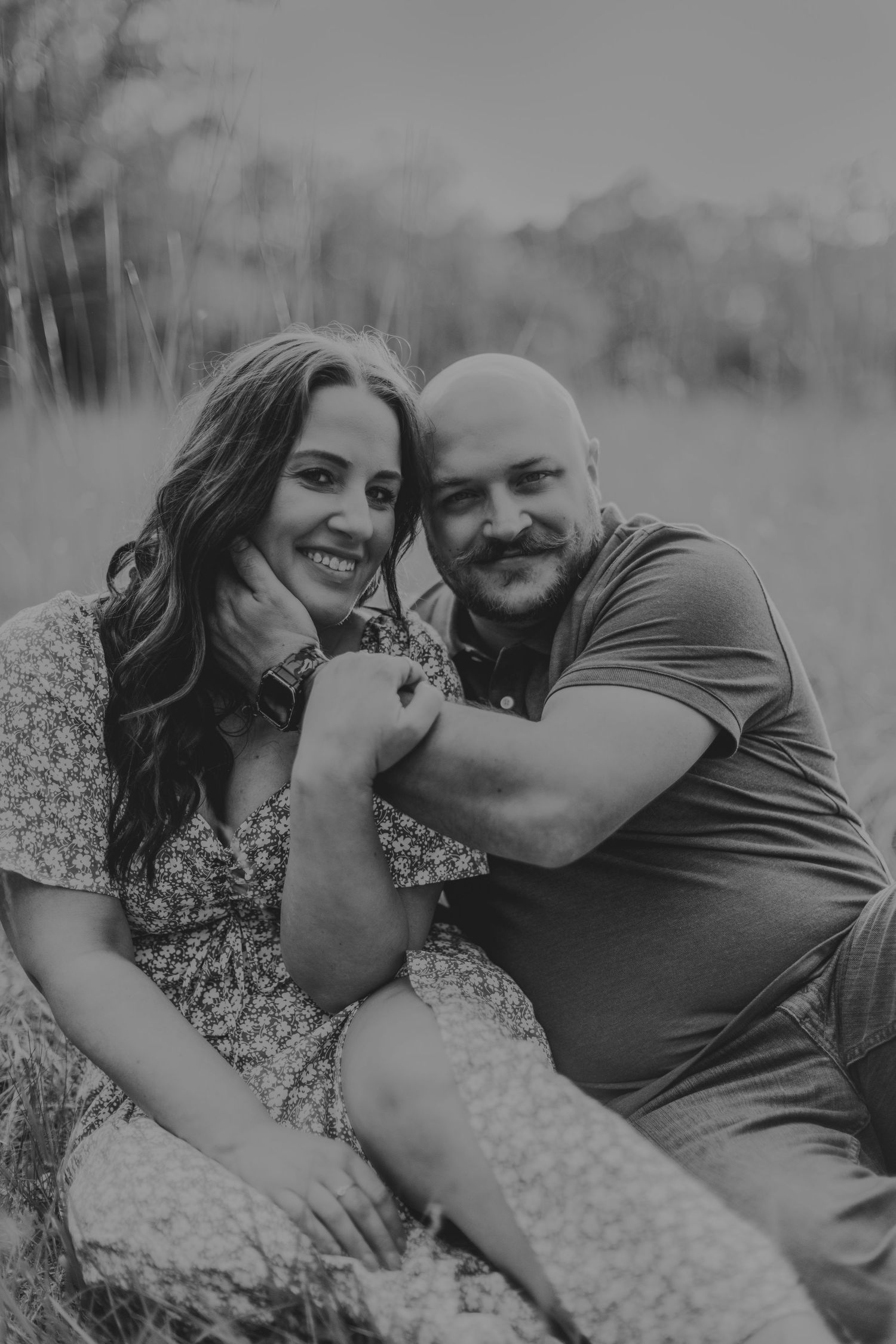 Black and white portrait captures candid laughter between couple on grassy field.