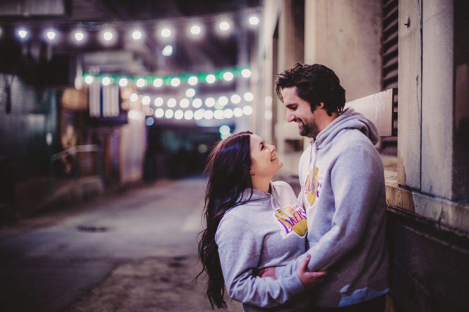 Couple in matching Lakers sweatshirts sharing an intimate moment under outdoor string lights.