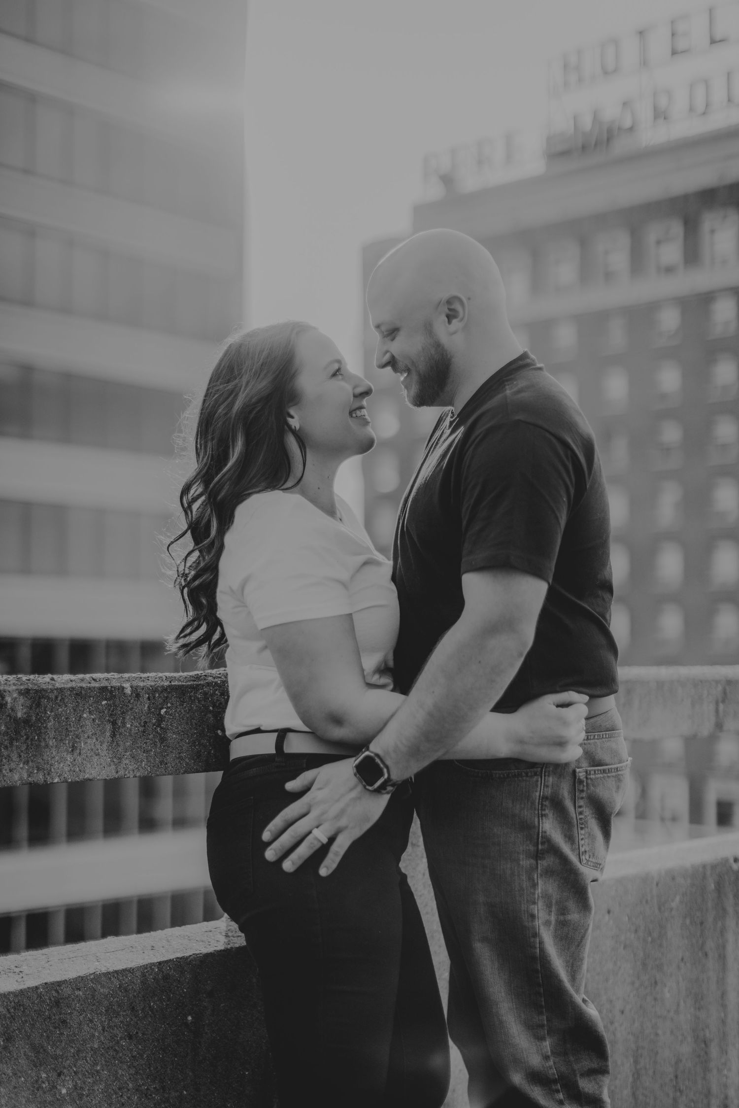 A black and white portrait of a couple sharing an intimate moment on a city rooftop.