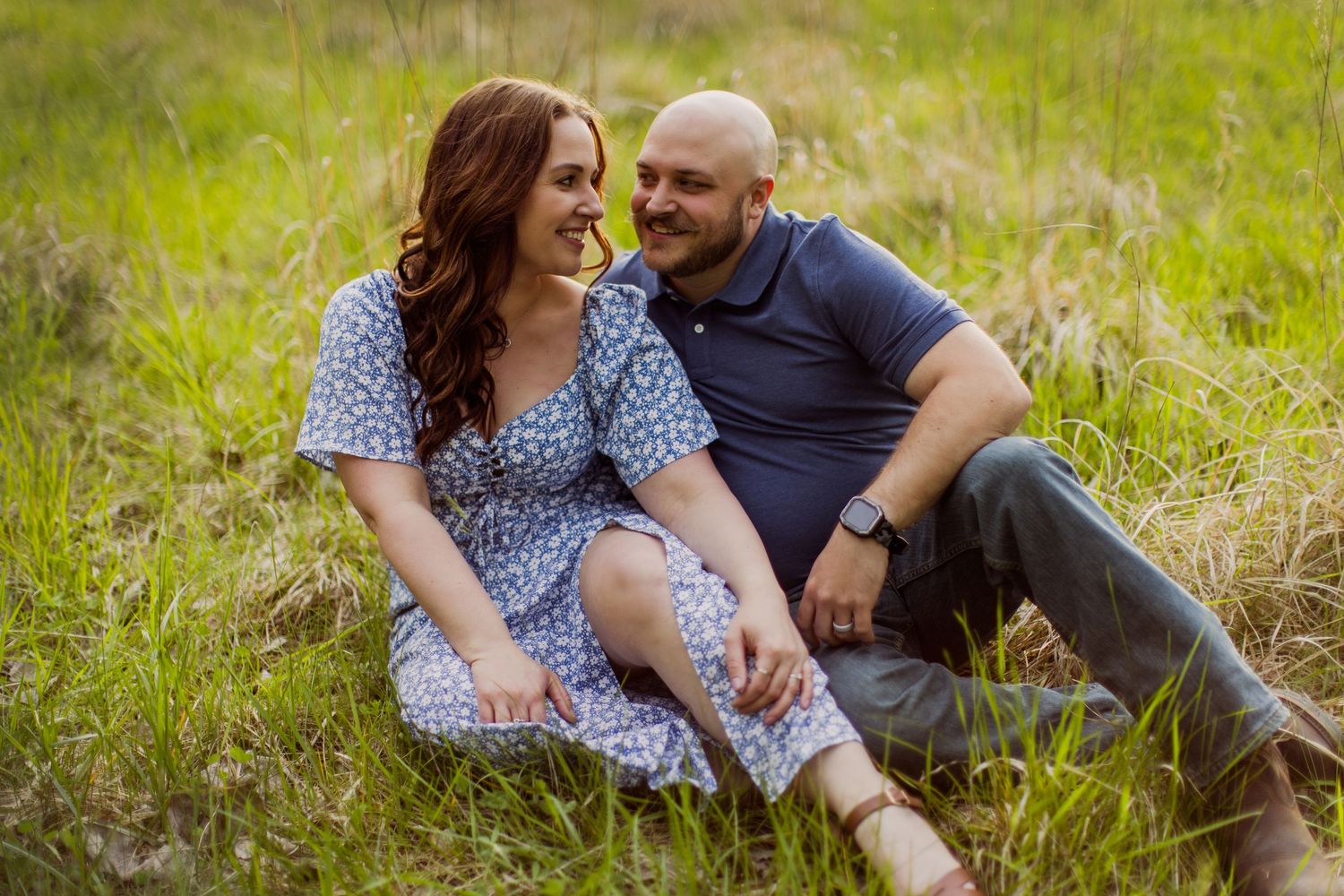 A couple shares joyful laughter while sitting together in a sunny meadow.
