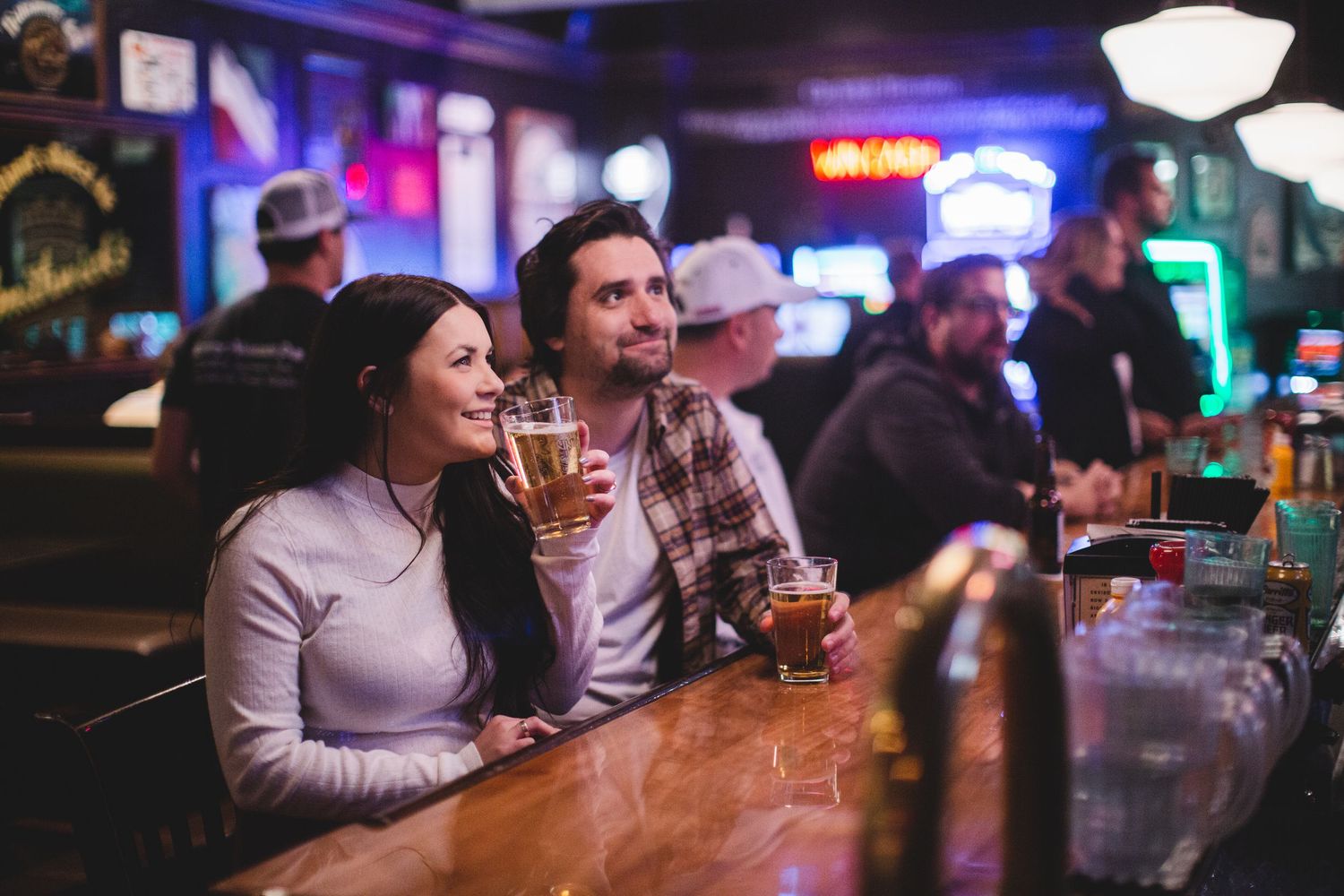 Patrons seated at a lively bar counter with colorful neon lighting in the background.