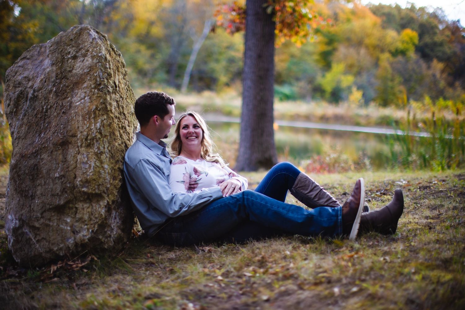 Couple sharing a joyful moment while sitting against a rock in a wooded area during fall.