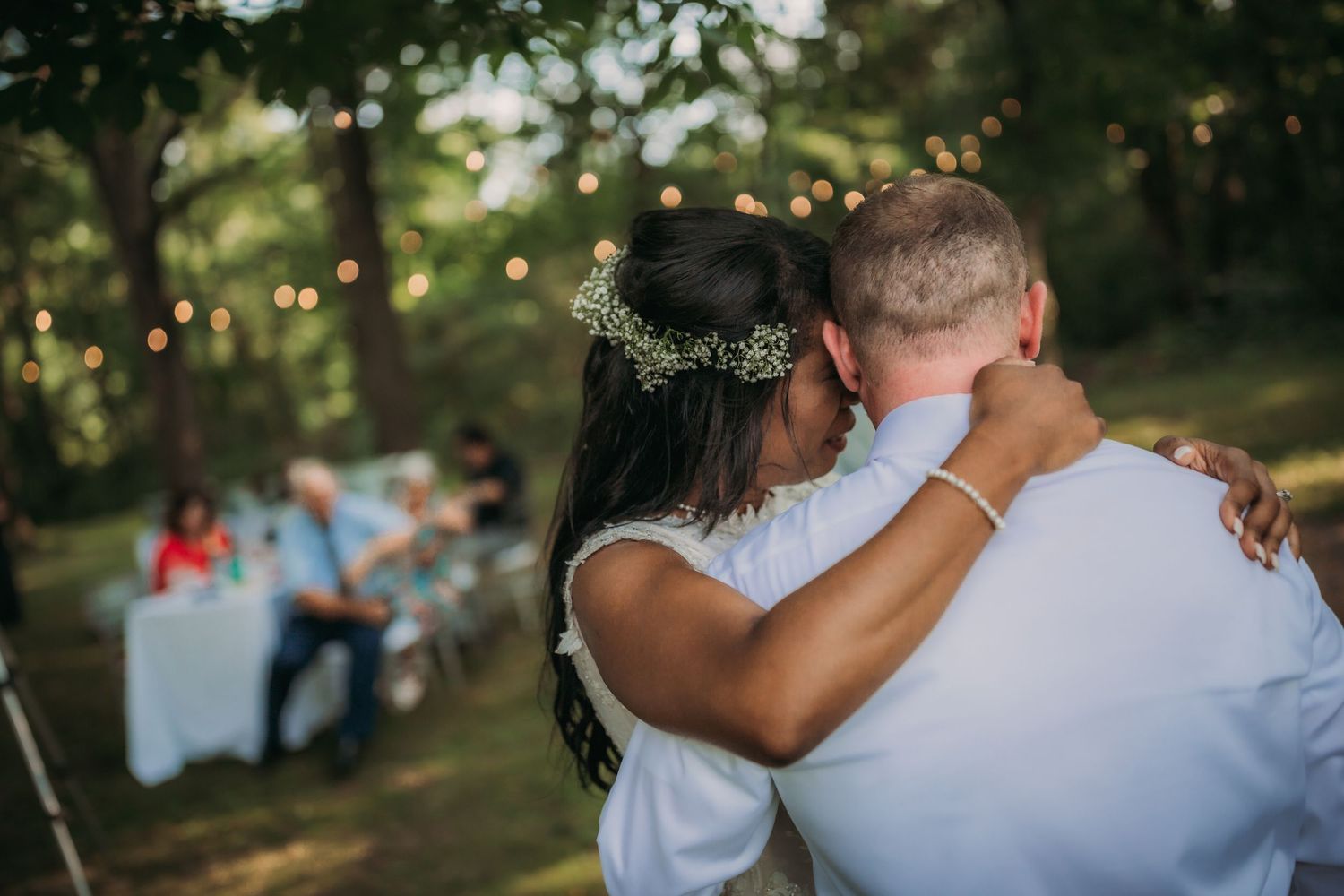 Couple dancing together at an outdoor reception with string lights and tables visible in the background.