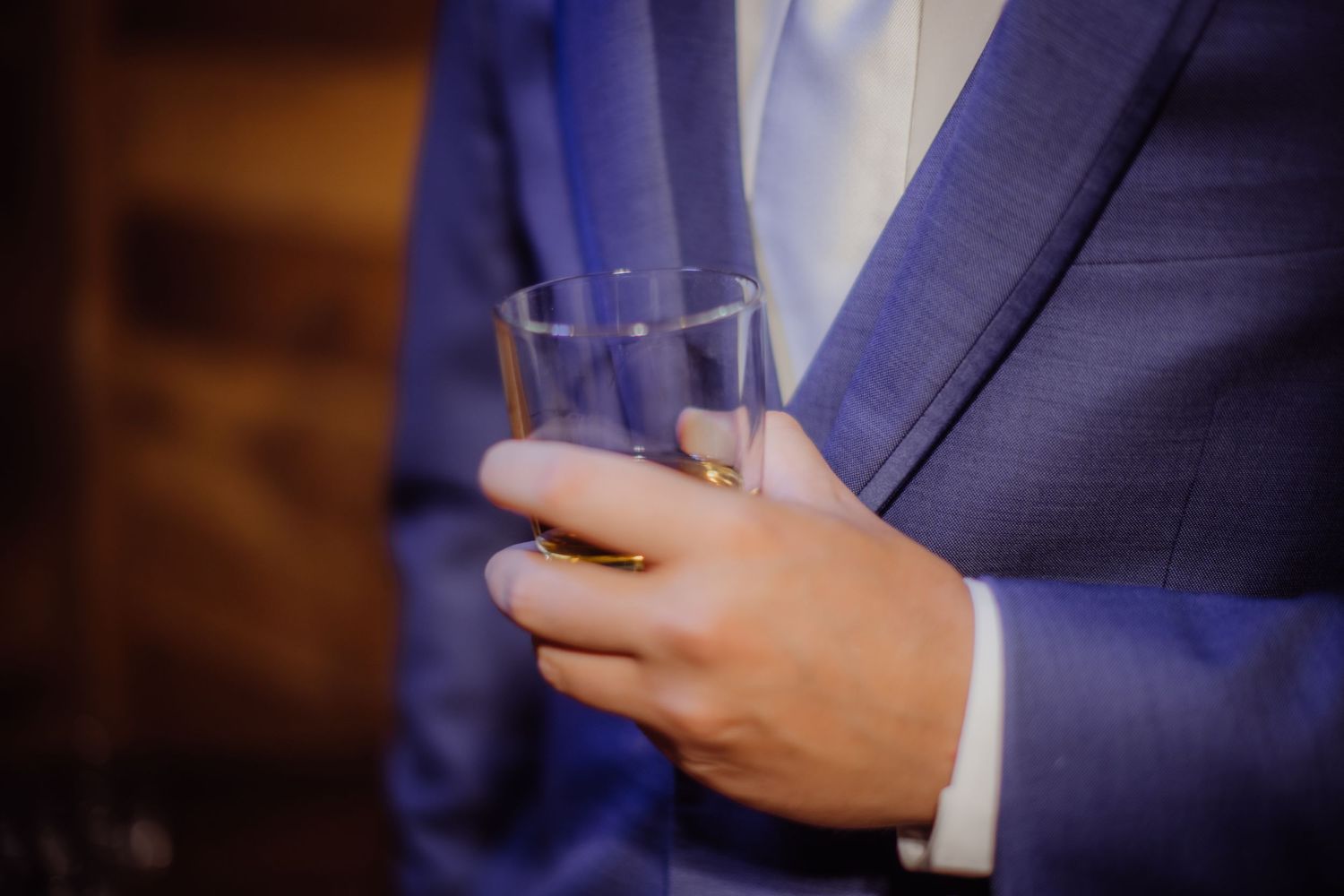 Person holding glass of spirits while wearing navy blue suit jacket.