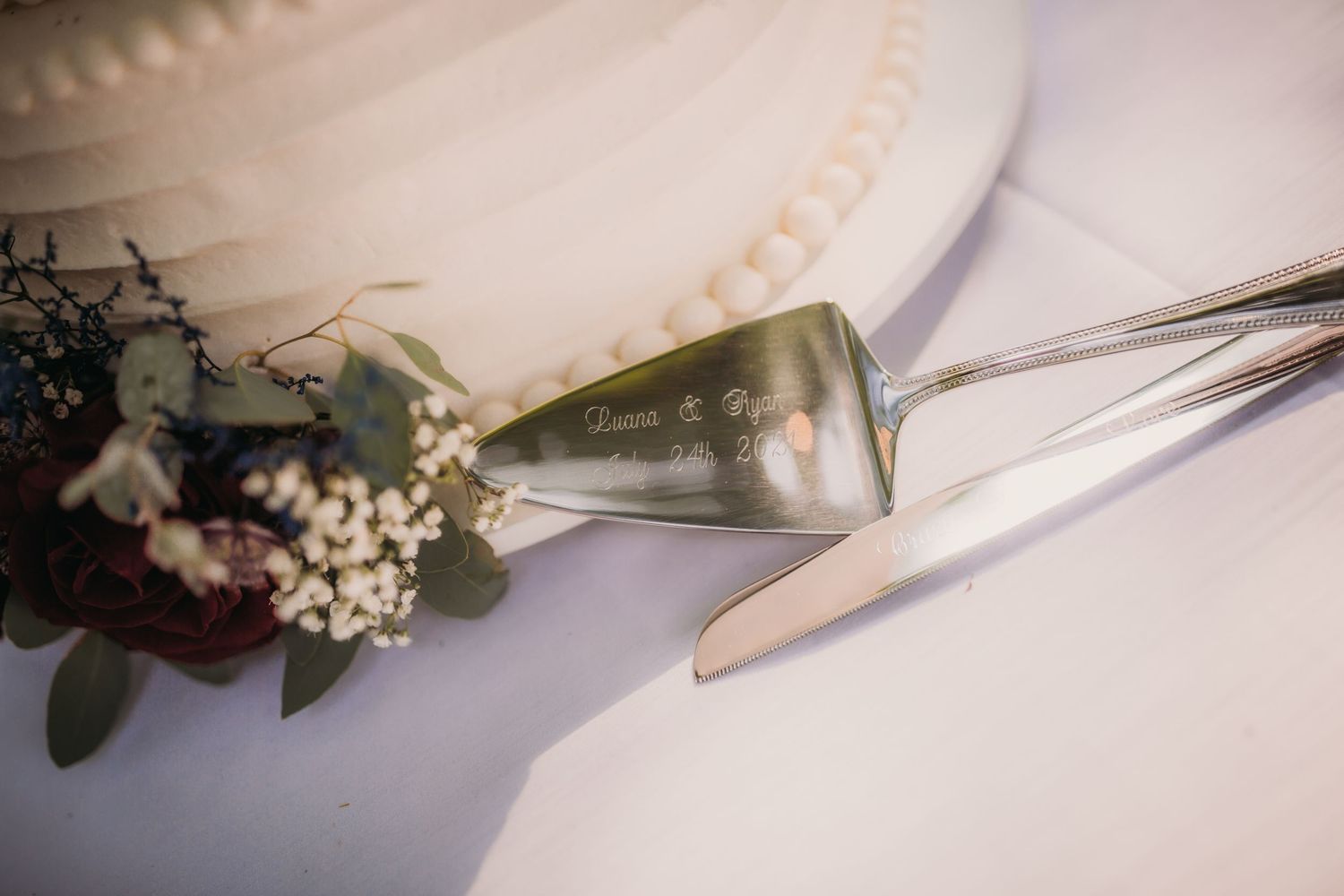 Close-up detail of wedding cake cutting utensils with decorative handles on white linens.