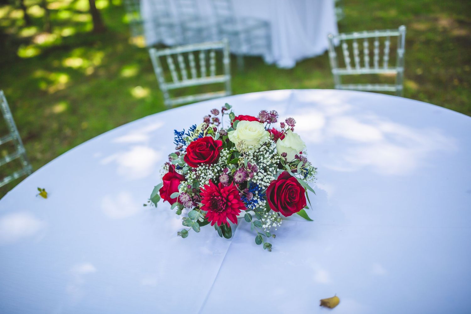 White wedding tables decorated with elegant red rose centerpieces in an outdoor setting.