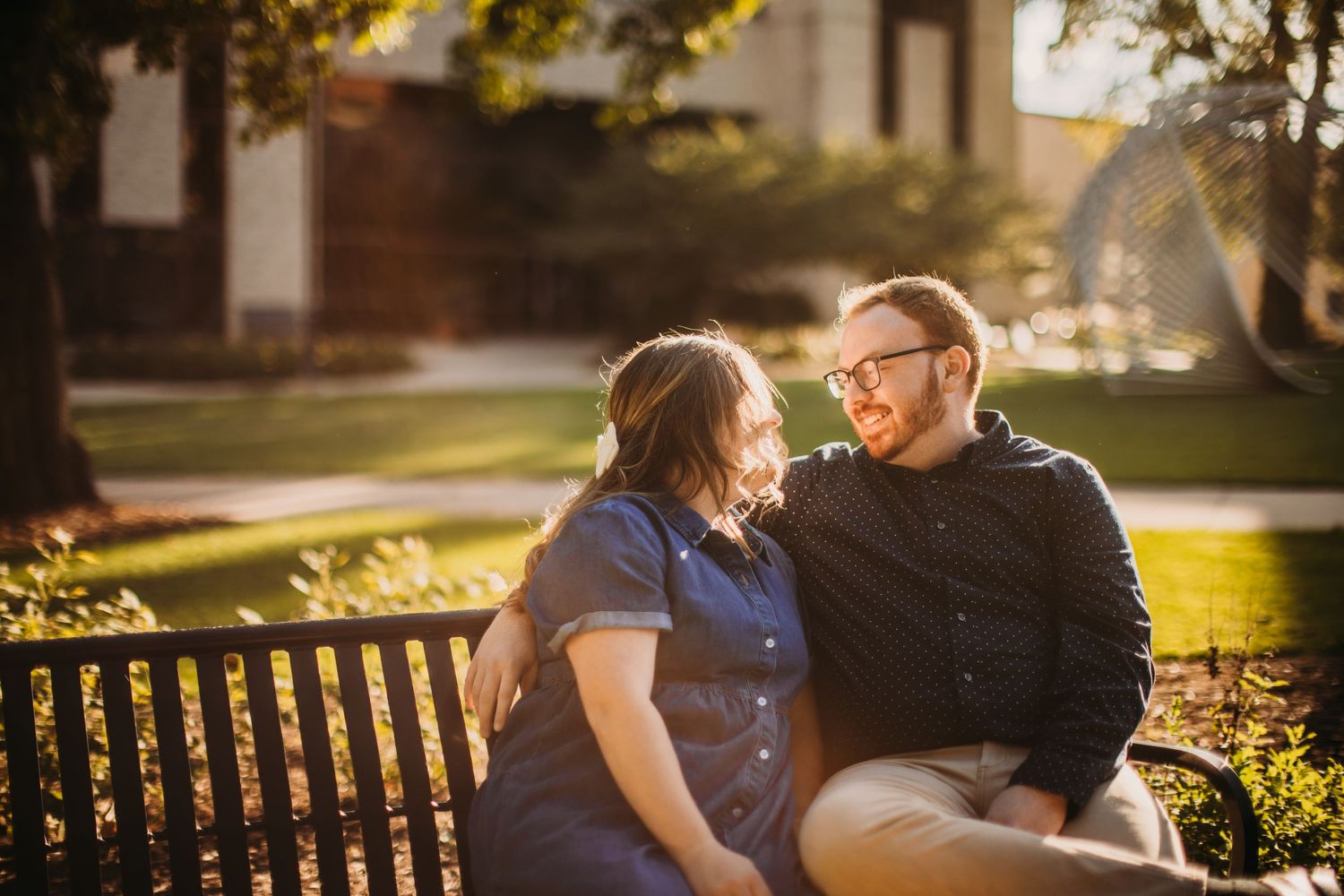 A couple shares a laugh while sitting together on a park bench during golden hour.
