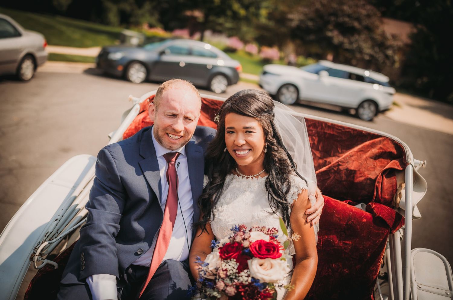 A wedding couple smiles together while seated in a classic white carriage.