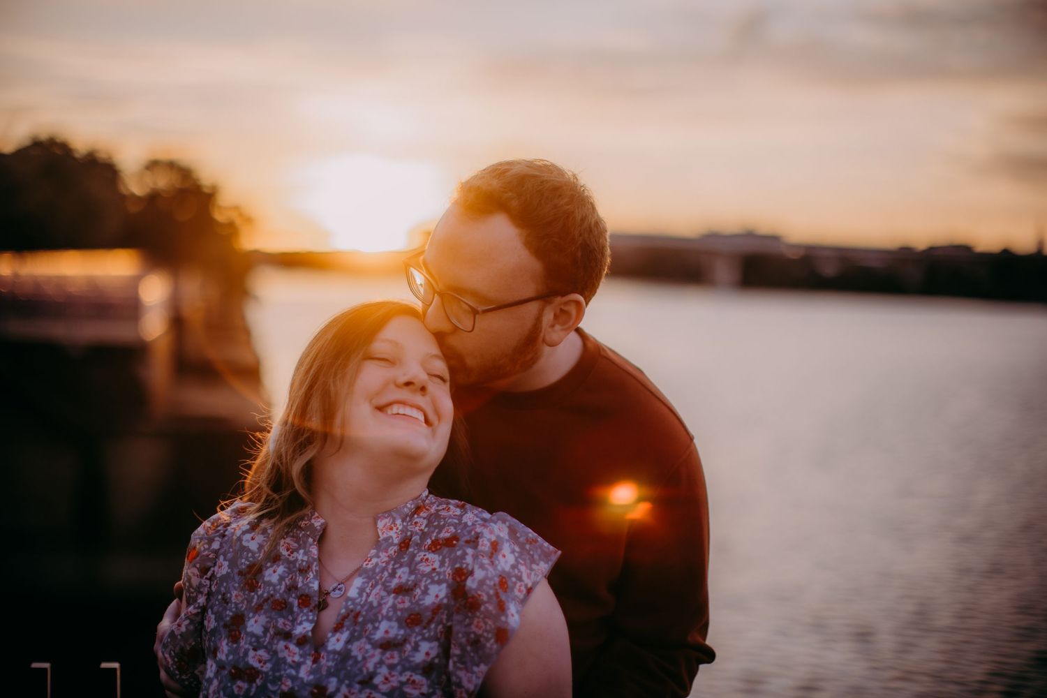 Intimate couple shares tender moment along riverside during glowing sunset.