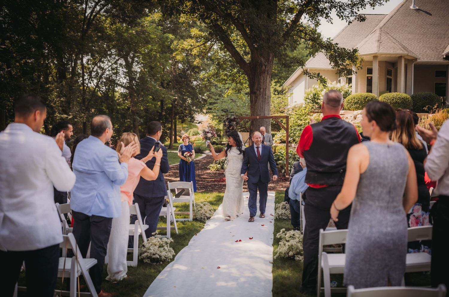 Wedding guests stand and mingle at an outdoor reception with trees and string lights.