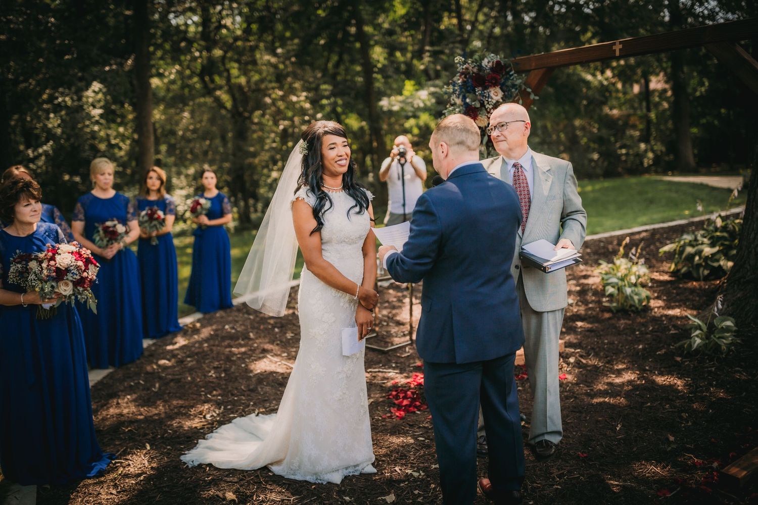 Outdoor wedding ceremony setup under trees with white chairs and blue accents.