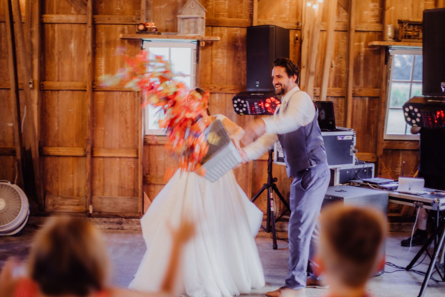 Wedding couple performs an energetic dance move during their reception in a rustic barn setting.