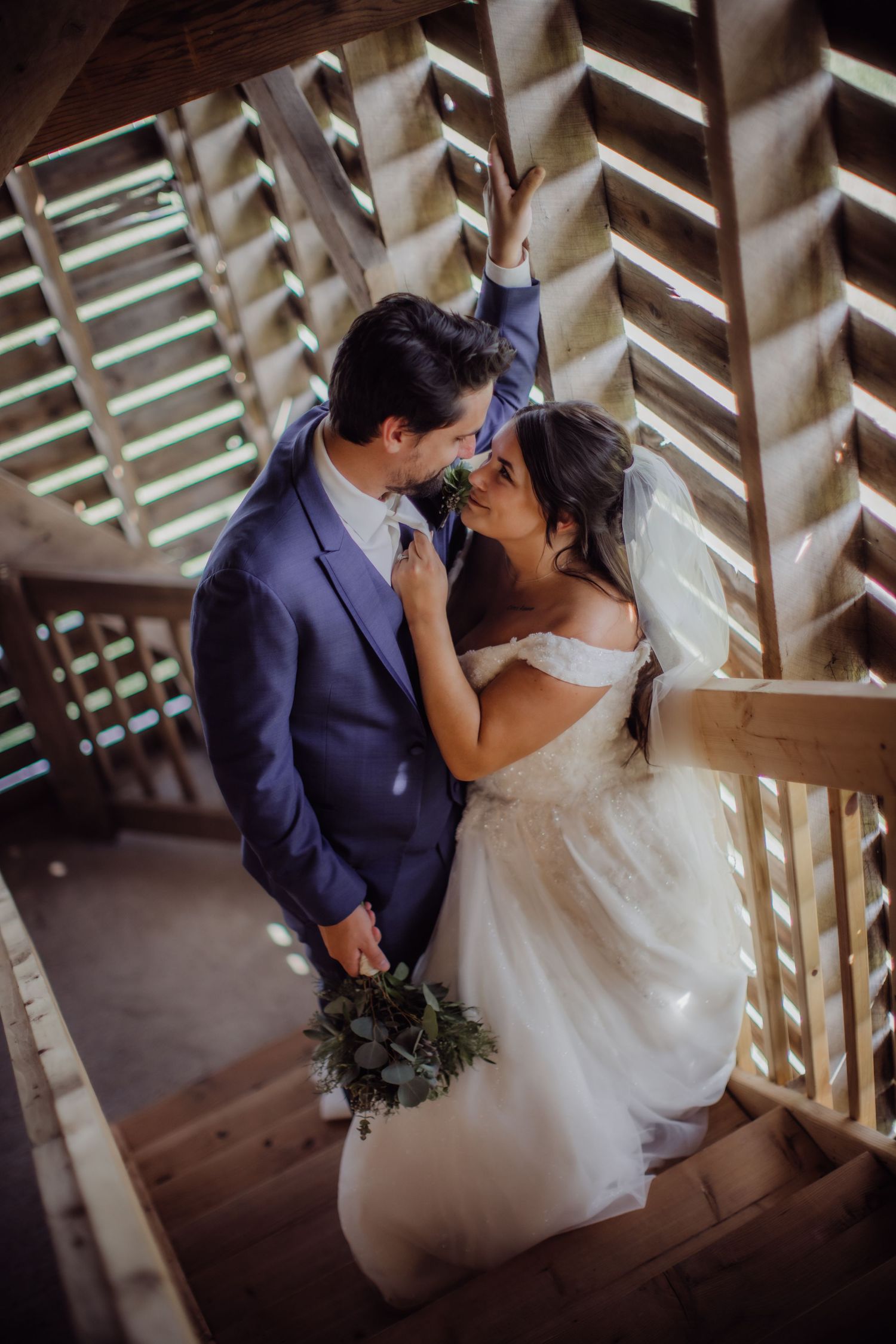 Bride and groom share a tender moment on rustic stairs with dramatic lighting.