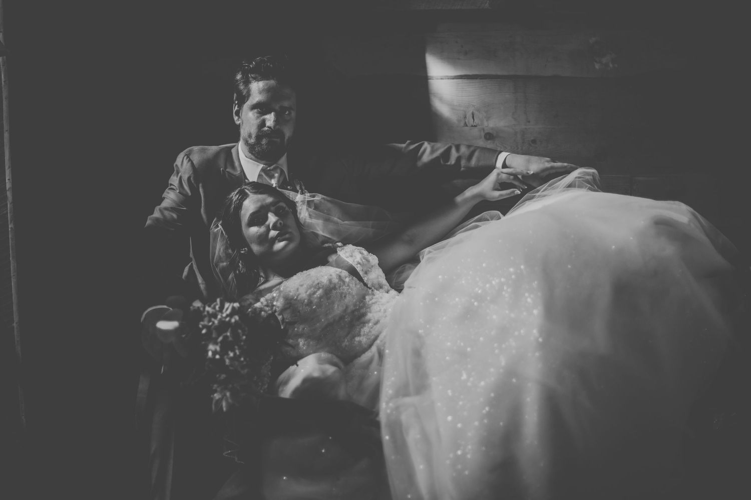 Dramatic black and white wedding photo of couple reclining on dark wooden stairs.