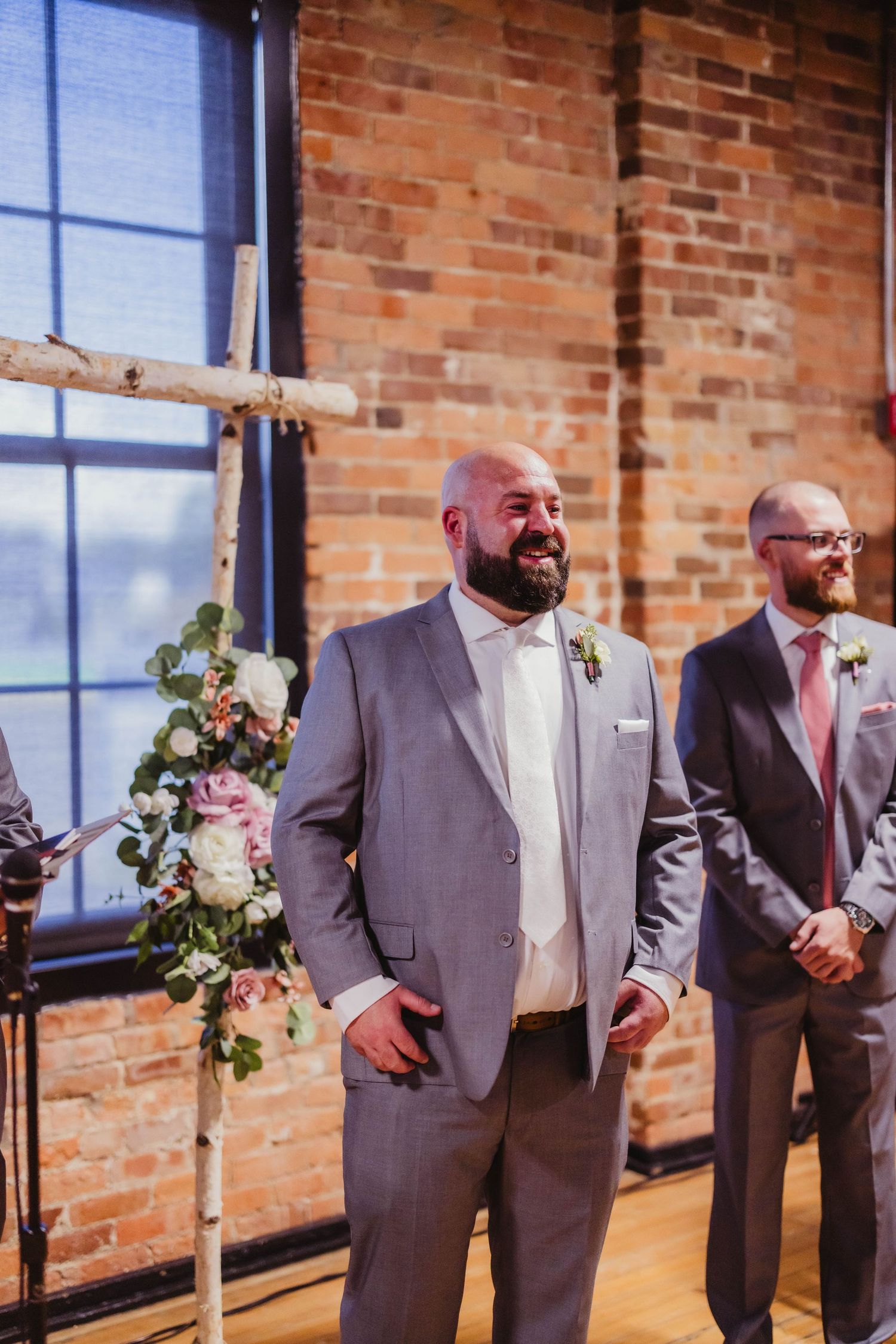 A groomsman in a grey suit stands at attention during a wedding ceremony.