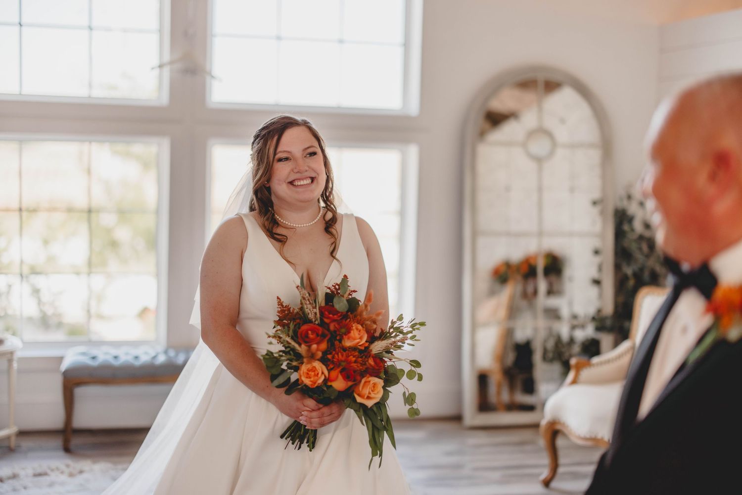 A couple shares an emotional first look in a sunlit room with elegant white decor and windows.