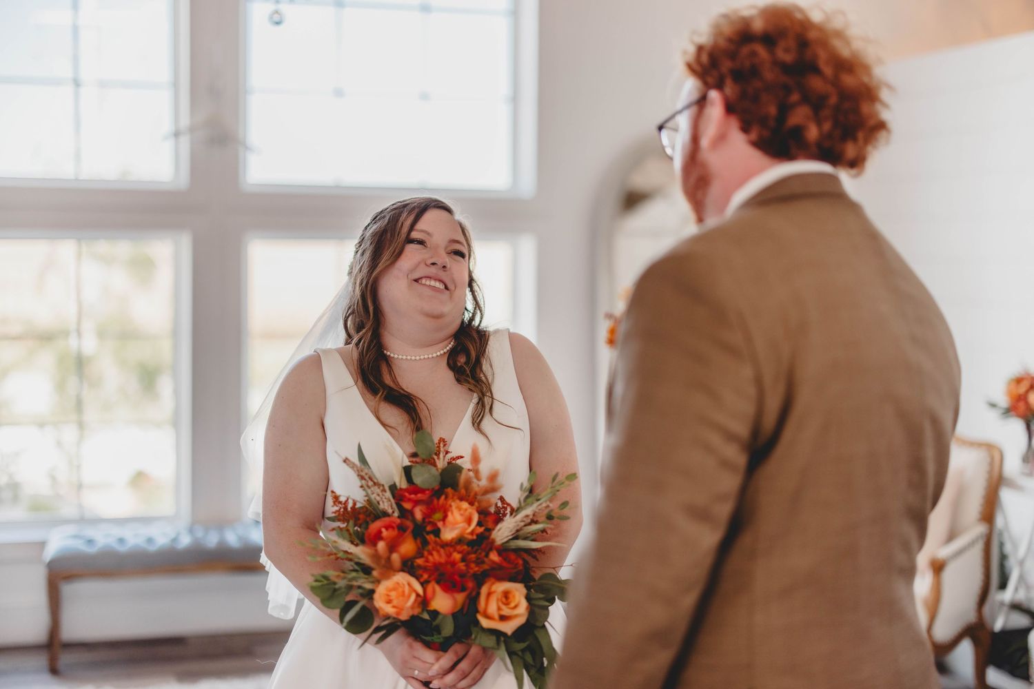 Wedding ceremony in bright indoor venue featuring elegant orange and red floral arrangements.