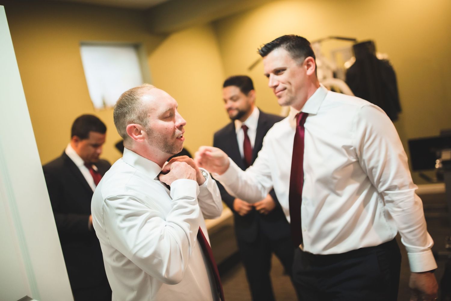 Group of people in formal wear interact while getting ready in a warmly lit room.
