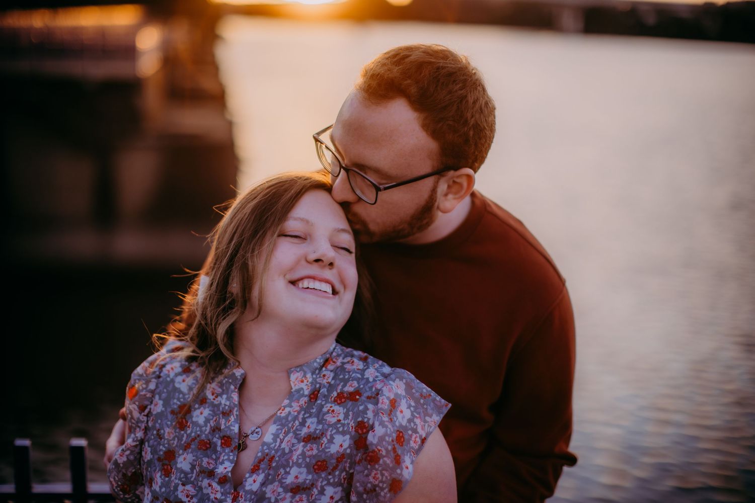Sweet candid moment captured between couple by water during sunset.