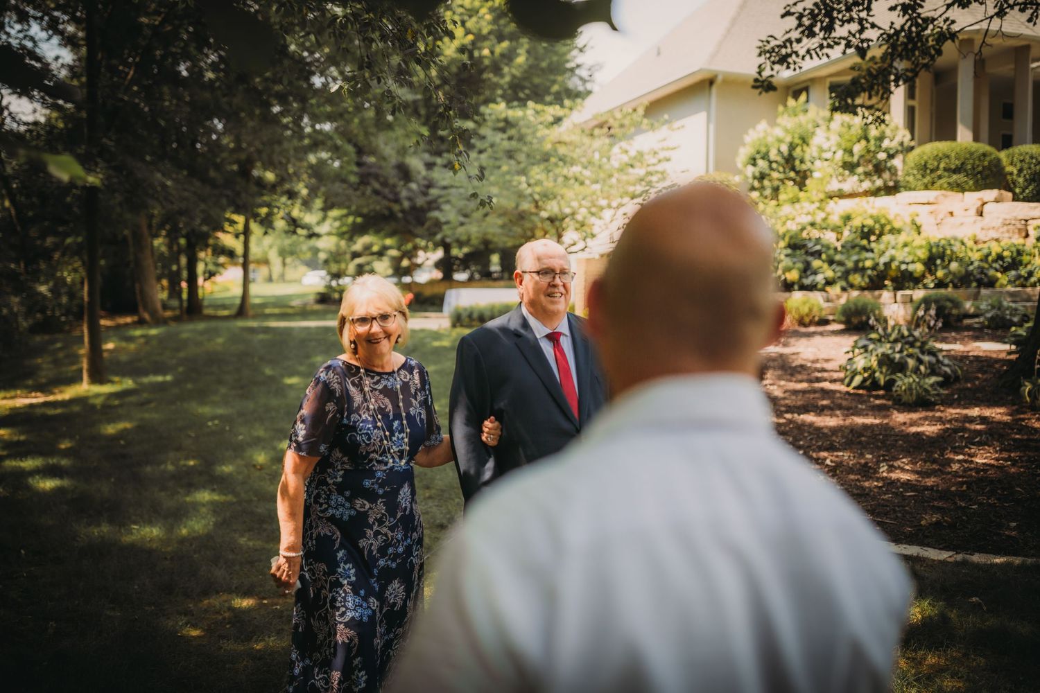 Wedding ceremony processional taking place on a sunny afternoon in a garden setting.
